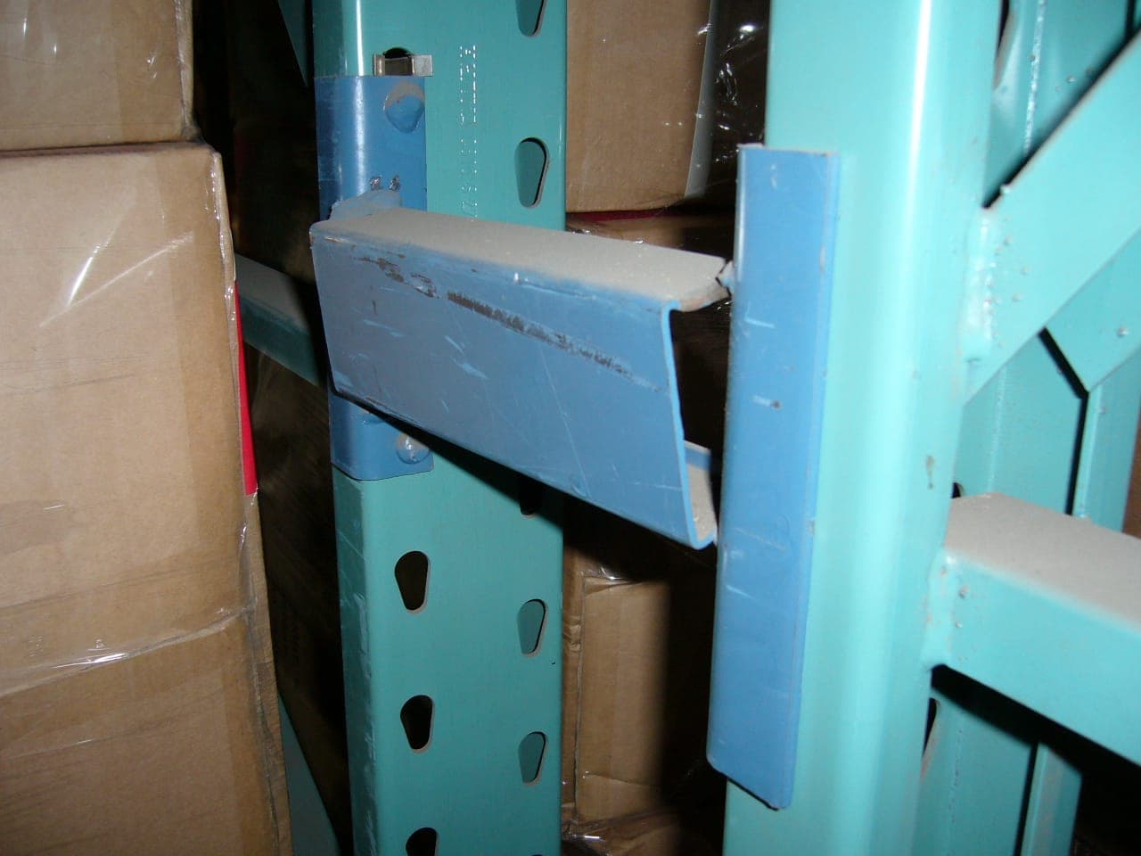 Gebruikte palletstelling van dichtbij: blauwe ligger met gebruikssporen in de lak, ingehaakt in de perforatie van een groene staander