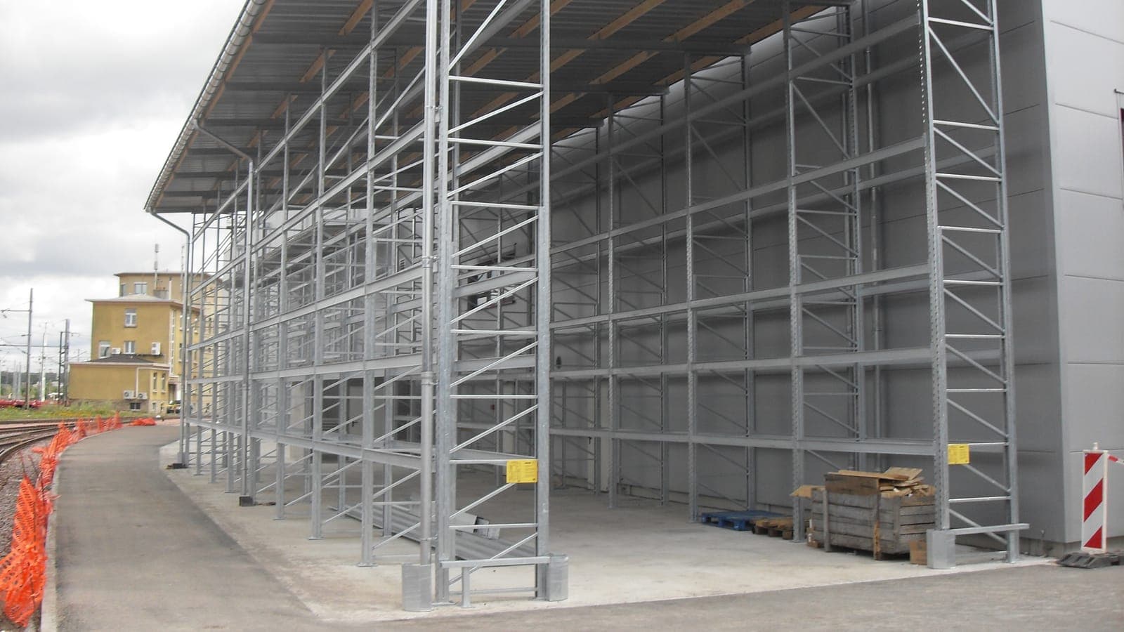 Nieuwe verzinkte palletstelling onder een overkapping, met gele belastingborden op de eindjukken en verankerde voetplaten